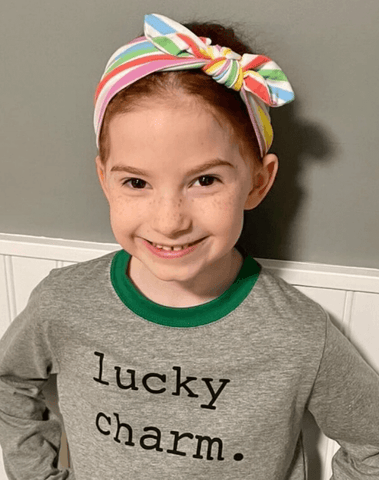 Girl is wearing a handmade knot headband featuring a rainbow print from By Bella Boutique.