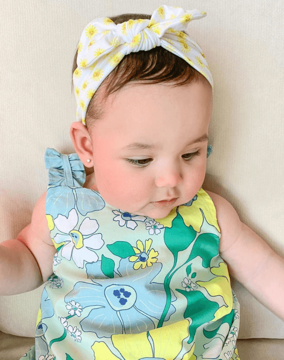 Baby girl is wearing the most comfortable headband featuring a sun pattern from By Bella Boutique.