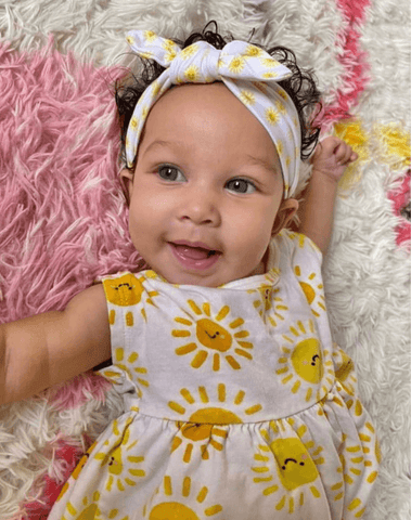 Baby girl is wearing a knotted head wrap featuring a sun print from By Bella Boutique.