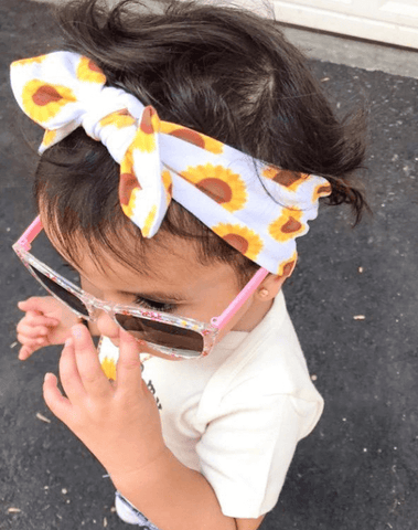 Baby girl is wearing a top knot headband featuring a cute sunflower pattern for little girls from By Bella Boutique.